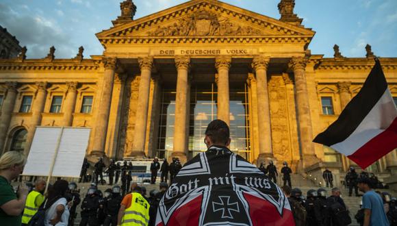 Un manifestante envuelto en una bandera del imperio alemán encara a policías antidisturbios que custodian el edificio del Reichstag. (Foto de John MACDOUGALL / AFP).