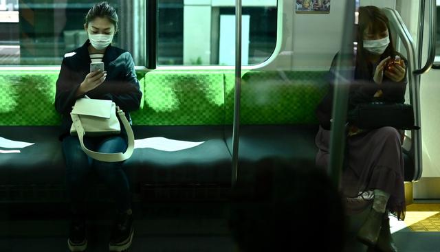 Las mujeres usan sus teléfonos en el tren de la línea Yamanote en Tokio el 8 de abril de 2020, el primer día del estado de emergencia. (CHARLY TRIBALLEAU / AFP).
