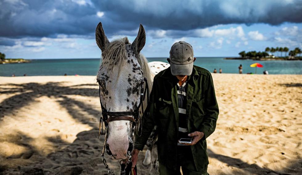Un hombre mira su teléfono móvil mientras camina con su caballo. (Foto de Yamil Lage / AFP)