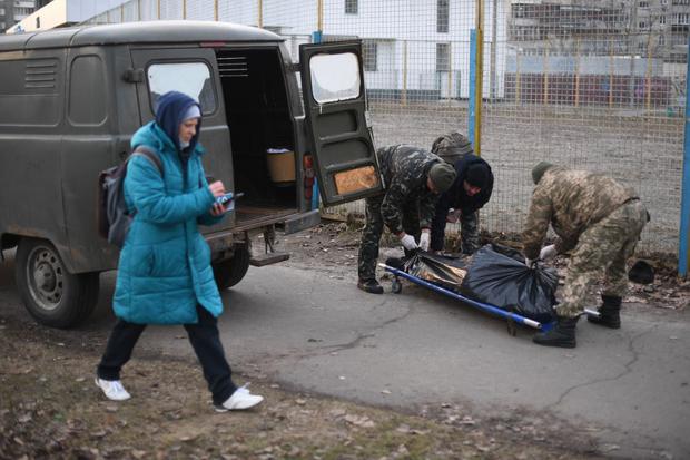 A woman walks as the Ukrainian military collects the body of a Ukrainian man who was shot when a Russian armored vehicle drove past him in northern Kiev on February 25, 2022. (DANIEL LEAL/AFP)