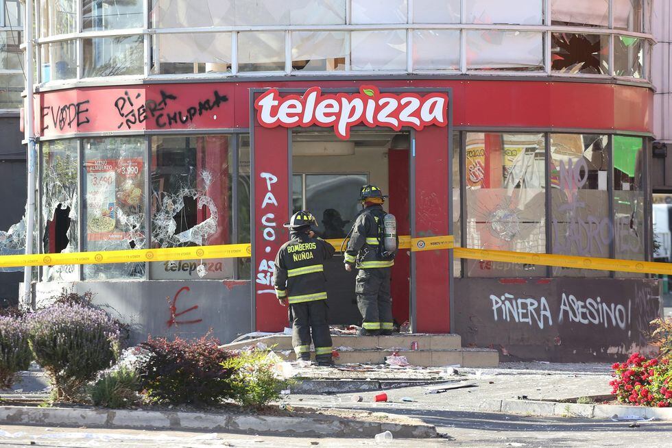 Personal de bomberos inspecciona un local de pizzas después de ser saqueado por manifestantes en Santiago. (EFE/ Elvis González).