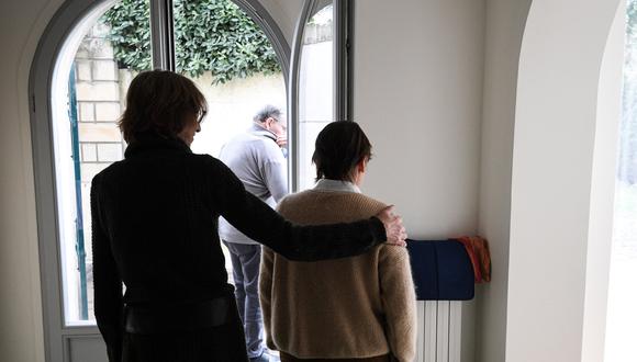 Una cuidadora ayuda a un anciano residente -uno de los tres enfermos de alzheimer del establecimiento- en una casa de L'Hay-les-Roses, en las afueras de París, el 17 de febrero de 2022, que funciona como alternativa al modelo tradicional de residencia. (Foto de ALAIN JOCARD / AFP)