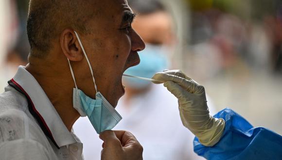 Un trabajador de la salud toma una muestra de hisopo de un hombre para detectar el coronavirus Covid-19 en el distrito de Huangpu, China, el 17 de agosto de 2022. (Héctor RETAMAL / AFP).