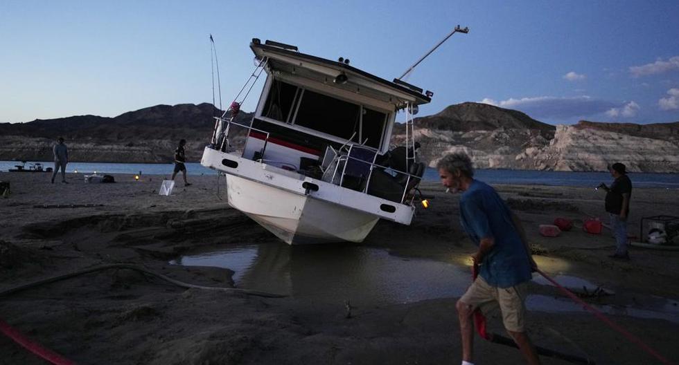 Craig Miller arrastra una manguera para tratar de desatascar su casa flotante, que quedó varada en el lago Mead al bajar el nivel de las aguas en medio de una sequía. Foto del 23 de junio del 2022. (AP Photo/John Locher).