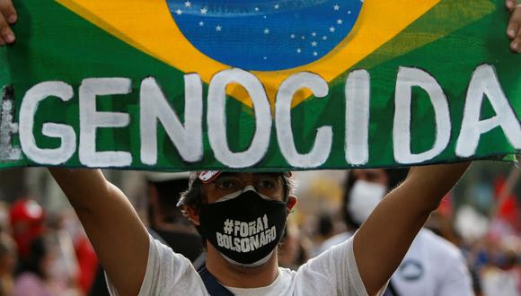 Un hombre sostiene una bandera de Brasil que dice "Genocida" durante una manifestación contra el manejo del presidente Jair Bolsonaro de la pandemia de coronavirus COVID-19 en Sao Paulo, el 3 de julio de 2021. (MIGUEL SCHINCARIOL / AFP).