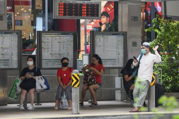 Las personas usan mascarillas para tratar de detener la propagación del coronavirus COVID-19 mientras esperan en una parada de autobús en Orchard Road en Singapur (Foto: Roslan Rahman / AFP)