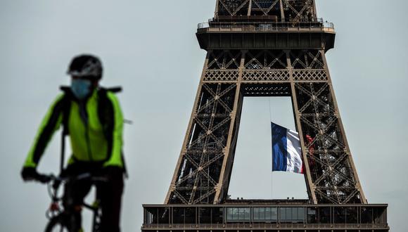Un hombre con una máscara facial monta su bicicleta mientras una bandera nacional francesa ondea en la Torre Eiffel el 11 de mayo de 2020, en plena pandemia de coronavirus. (PHILIPPE LOPEZ / AFP).