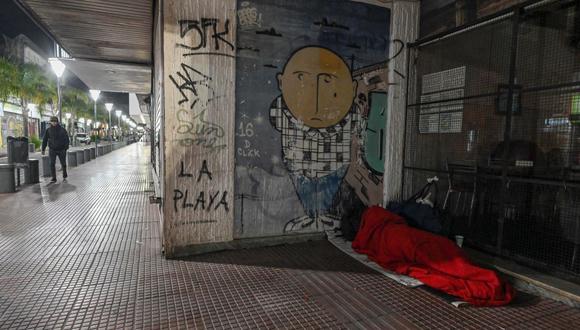 Una persona sin hogar duerme en la calle mientras los miembros de la ONG "Dando una mano" ayudan a los voluntarios del grupo "La Sachetera" a repartir alimentos y mantas en Buenos Aires, Argentina, el 20 de junio de 2022. (LUIS ROBAYO / AFP).