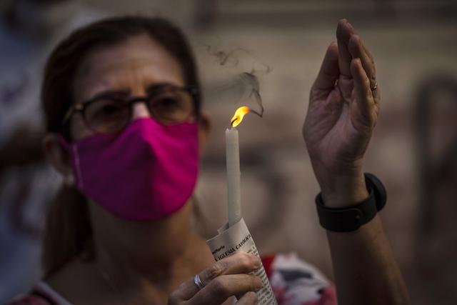 Una mujer que usa mascarilla para protegerse del coronavirus sostiene una vela encendida durante una misa católica transmitida por radio en honor a la Virgen de la Caridad del Cobre, en su fiesta en La Habana, Cuba. (AP/Ramon Espinosa).