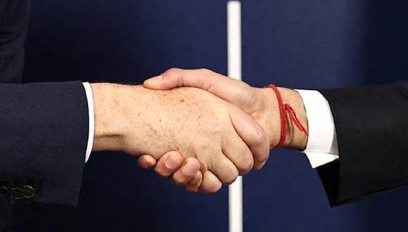 Dos personas se dan la mano. (Foto de HENRY NICHOLLS / POOL / AFP)