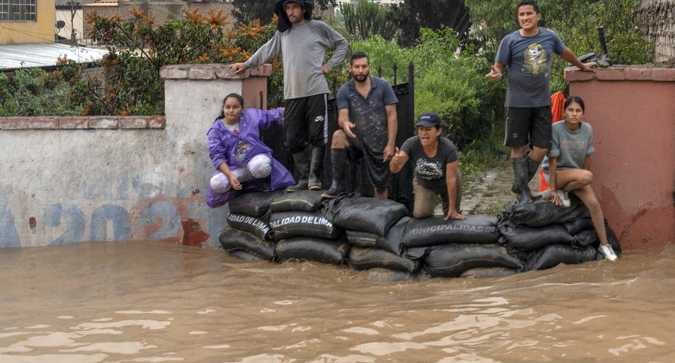 La gente mira detrás de bolsas de arena mientras el agua inunda la principal vía de acceso desde Lima al interior del país en los Andes luego de fuertes lluvias en Chaclacayo, el 15 de marzo de 2023.(Foto de Cris BOURONCLE / AFP).