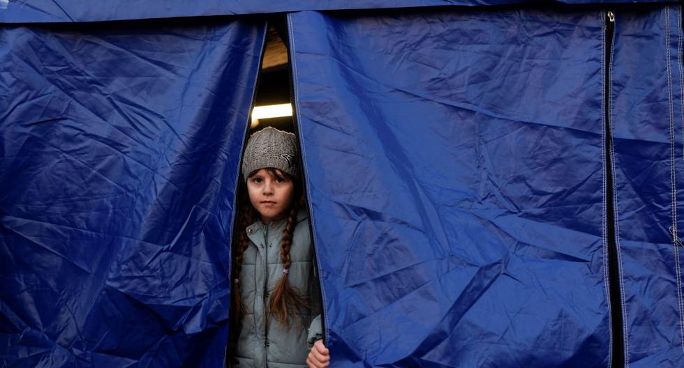 Una niña ucraniana mira desde una tienda de campaña mientras espera la reubicación después de cruzar la frontera entre Ucrania y Rumania en Siret, el 19 de marzo de 2022. (Armando NIMANI / AFP).