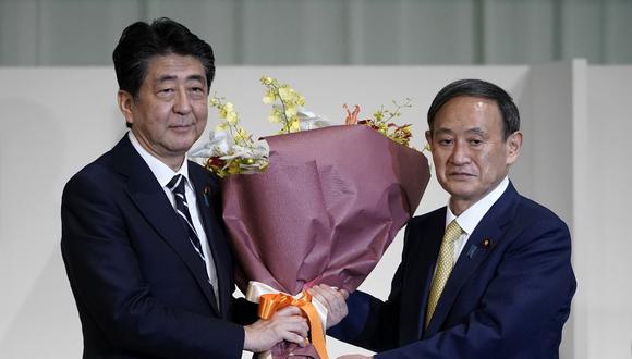 El primer ministro saliente de Japón, Shinzo Abe, presenta flores al nuevo líder del Partido Liberal Democrático (PLD), Yoshihide Suga, después de que este último fuera elegido como nuevo jefe del partido gobernante de Japón. (Eugene Hoshiko / POOL / AFP)