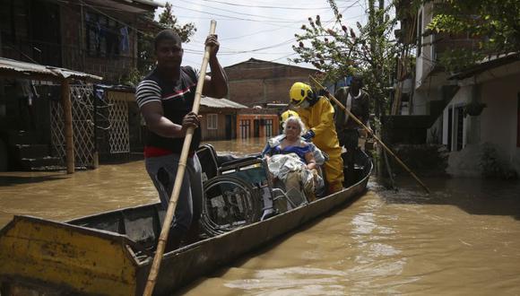 Residentes y bomberos utilizan una canoa para evacuar a una mujer en silla de ruedas de las calles inundadas del barrio Playa Renaciente después de que fuertes lluvias provocaran el desbordamiento del río Cauca e inundaran cientos de viviendas en Cali.