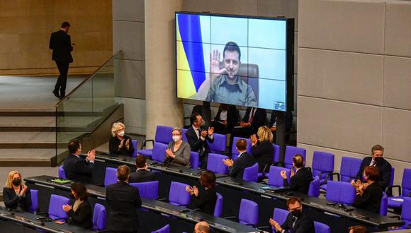 Miembros del gobierno de Alemania, entre ellos el canciller alemán Olaf Scholz (abajo centro), aplauden cuando el presidente de Ucrania, Volodymyr Zelensky, aparece en una pantalla para emitir un mensaje. (Tobías SCHWARZ / AFP).