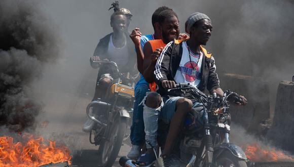 Hombres en motocicletas pasan quemando neumáticos durante una manifestación tras la dimisión de su primer ministro Ariel Henry, en Puerto Príncipe, Haití, el 12 de marzo de 2024. (Foto de Clarens SIFFROY / AFP)