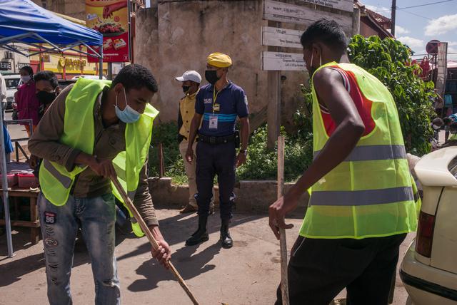 Un oficial observa cómo los hombres con chaleco amarillo barren la calle después de ser detenidos por agentes de policía por no usar sus máscaras faciales. (Foto: AFP)