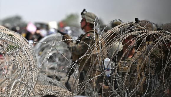 Soldados de Estados Unidos hacen guardia detrás de un alambre de púas mientras los afganos se reúnen en una carretera cerca del aeropuerto de Kabul el 20 de agosto de 2021. (Wakil KOHSAR / AFP).