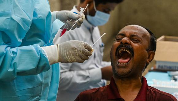 Un trabajador de la salud toma una muestra de un hisopo de un hombre para una prueba de coronavirus Covid-19 en un centro de salud en Nueva Delhi, India. (Foto de Prakash SINGH / AFP).