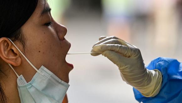 Un trabajador de la salud toma una muestra de hisopo de una mujer para la prueba del coronavirus Covid-19 en el distrito de Huangpu, Shanghai, el 17 de agosto de 2022. (Héctor RETAMAL / AFP).