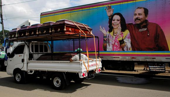 Un carro con ataúdes pasa junto a una pancarta del presidente de Nicaragua Daniel Ortega y su esposa y compañera de fórmula Rosario Murillo. (OSWALDO RIVAS / AFP).