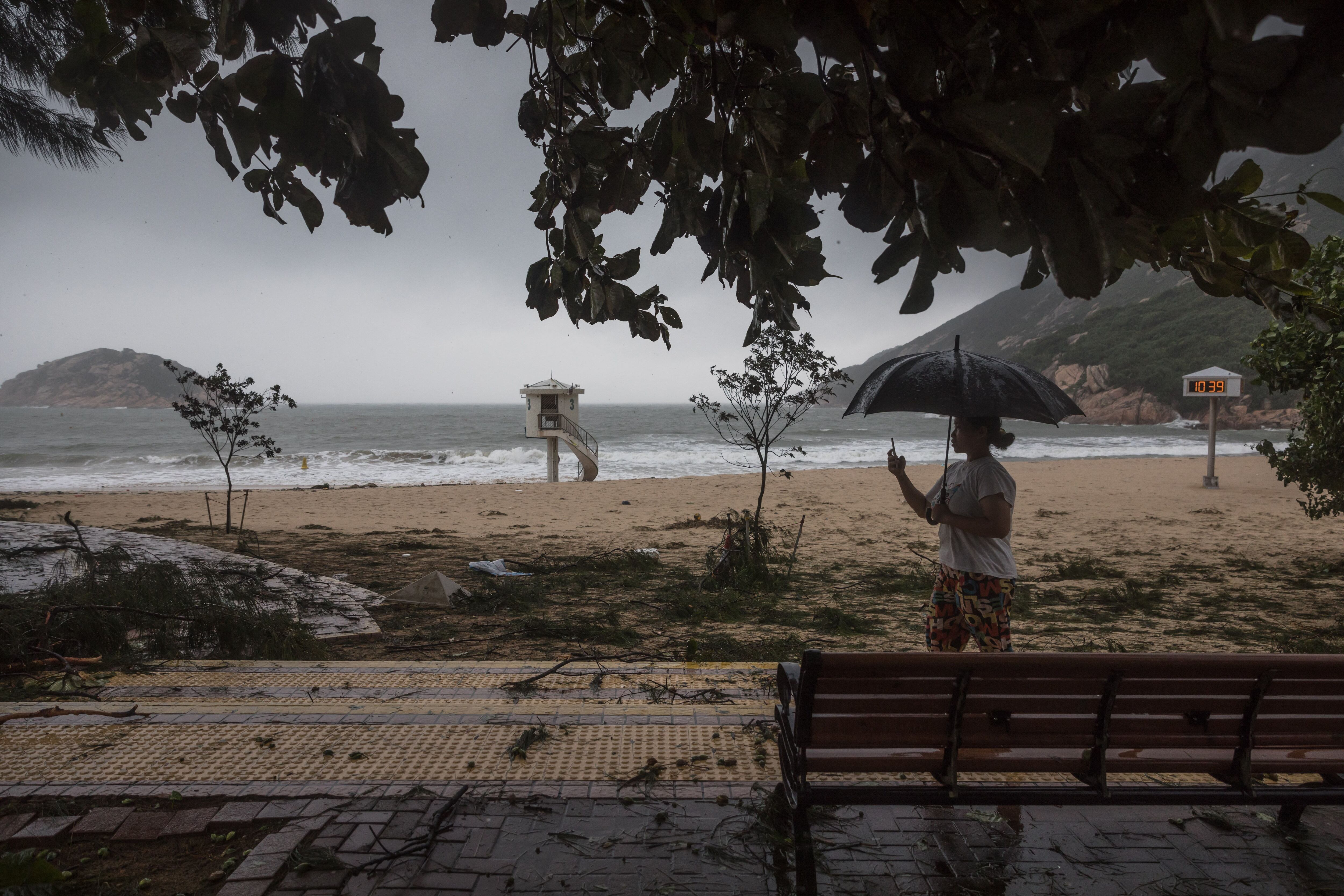 A woman films a beach covered in tree branches after Typhoon Saola in a Hong Kong coastal village on September 2, 2023. (Photo by DALE DE LA REY / AFP)