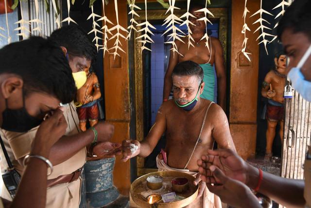 Un sacerdote del templo entrega cenizas sagradas a los residentes mientras ofrecen oraciones por la candidata demócrata a la vicepresidencia de Estados Unidos, Kamala Harris, en su aldea ancestral de Thulasendrapuram en el estado de Tamil Nadu, en el sur de la India. (AFP / Arun SANKAR).