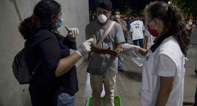 Dos mujeres dan indicaciones y echan alcohol a un joven (c) como medida de prevención ante el coronavirus.  (Foto: EFE/ Jorge Torres).
