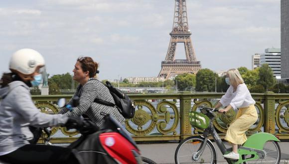 Una mujer usa una mascarilla protectora mientras cruza en bicicleta el puente Pont Mirabeau, cerca de la Torre Eiffe en París. (Foto: Archivo/ Ludovic MARIN / AFP)