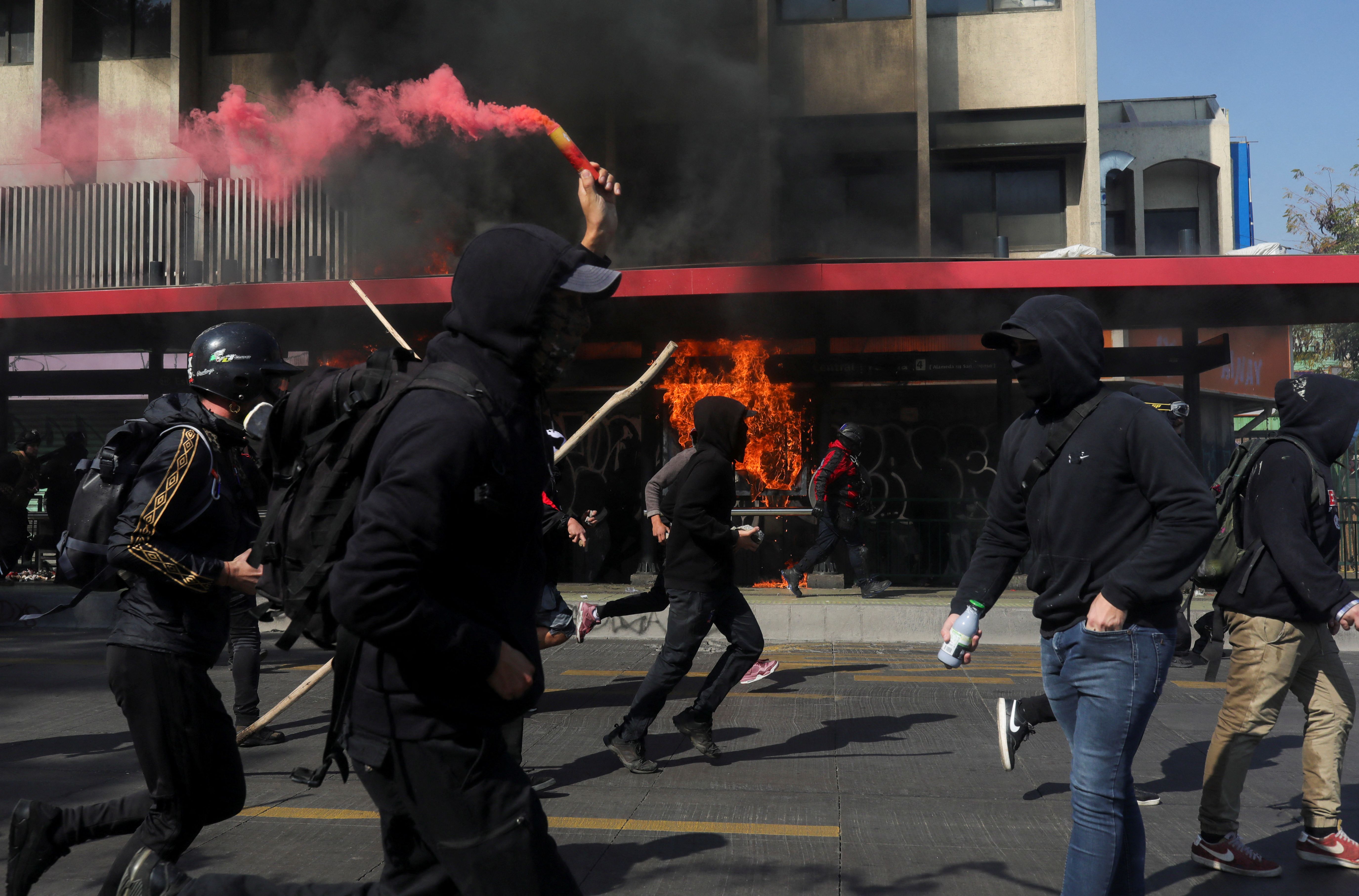 Fire burns at a bus stop as protesters run during the May Day demonstration in Santiago, Chile.