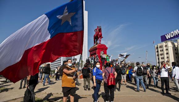 Un manifestante sostiene una bandera nacional de Chile durante una protesta contra el gobierno del presidente de Chile, Sebastián Piñera, junto al monumento al General Baquedano -pintado de rojo- en la Plaza Italia, en Santiago el 16 de octubre de 2020 (Foto de Martin Bernetti / AFP)