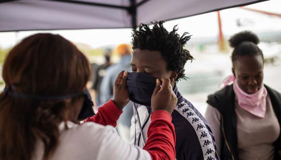 Un empleado de un centro comercial ayuda a un cliente a ponerse una mascarilla en la entrada de un centro comercial en Alexandra, Johannesburgo, en medio de la emergencia por el coronavirus en Sudáfrica. (Foto: Michele Spatari / AFP)