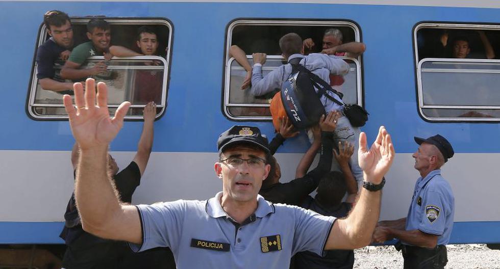 Un polic&iacute;a trata de detener a los refugiados que escalan por las ventanillas de los vagones para para subir a bordo de un tren. (Foto: EFE)