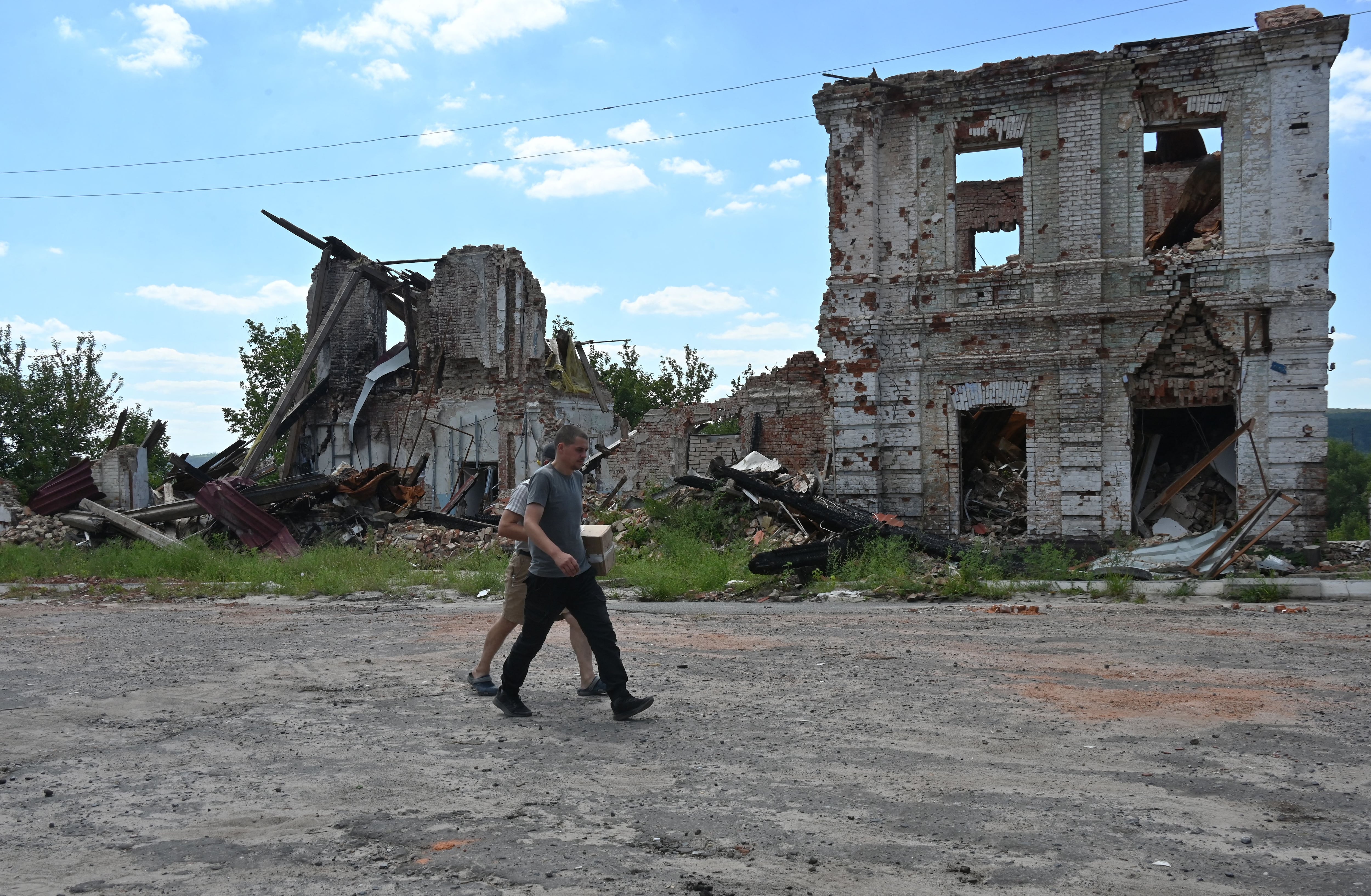 Local residents walk past a destroyed building in the city of Kupiansk, Kharkiv region, on August 17, 2023, amid the Russian invasion of Ukraine.  (Photo by SERGEY BOBOK / AFP).