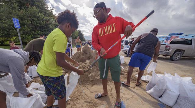 Jawan Williams saca arena para un saco de arena que sostiene su hijo Jayden Williams, antes de que el huracán Ida toque tierra en el Centro Cívico Frederick Sigur en Chalmette, Luisiana, que forma parte del área metropolitana del Gran Nueva Orleans. (AP/ Matthew Hinton).