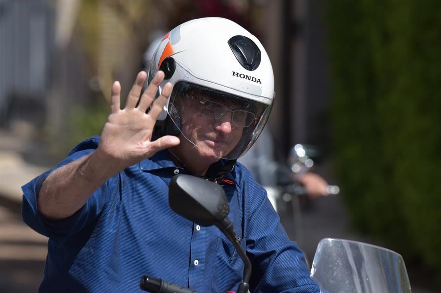El presidente de Brasil, Jair Bolsonaro, saluda este sábado mientras circula en motocicleta por una avenida de Brasilia (Brasil). Bolsonaro, de 65 años, ha dado negativo en un nuevo examen de coronavirus. (EFE/Andre Borges).