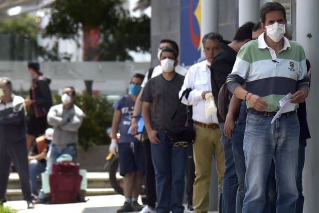 Un grupo de hombres con mascarillas como medida preventiva contra la propagación del nuevo coronavirus COVID-19, haciendo cola esperando su turno para ingresar a un banco en Bogotá (Foto: Raúl Arboleda / AFP)