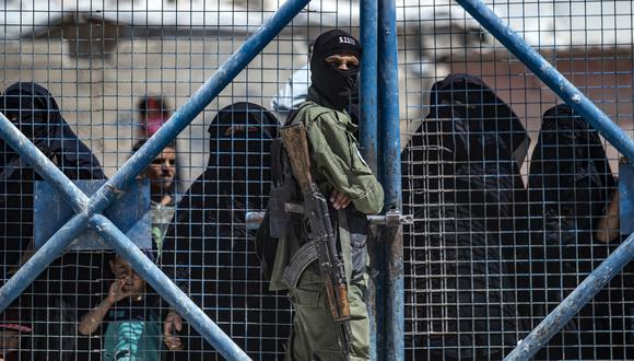 Un combatiente de las Fuerzas Democráticas Sirias (SDF) vigila una puerta mientras las mujeres sirias esperan dentro del campamento de al-Hol, dirigido por los kurdos. (Foto: Delil SOULEIMAN / AFP)