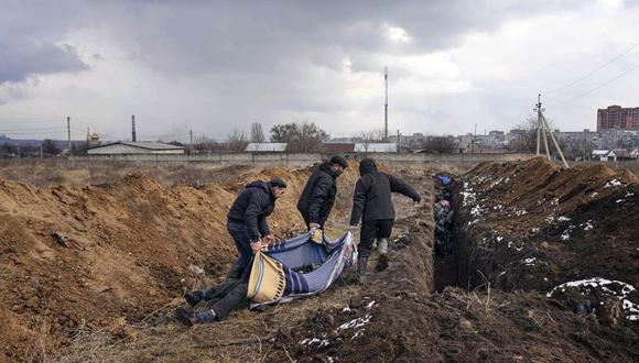 Tres individuos arrastran cadáveres para ser depositados en una larga fosa común en las afueras de Mariúpol (Ucrania) el 9 de marzo del 2022. (AP Photo/Evgeniy Maloletka).