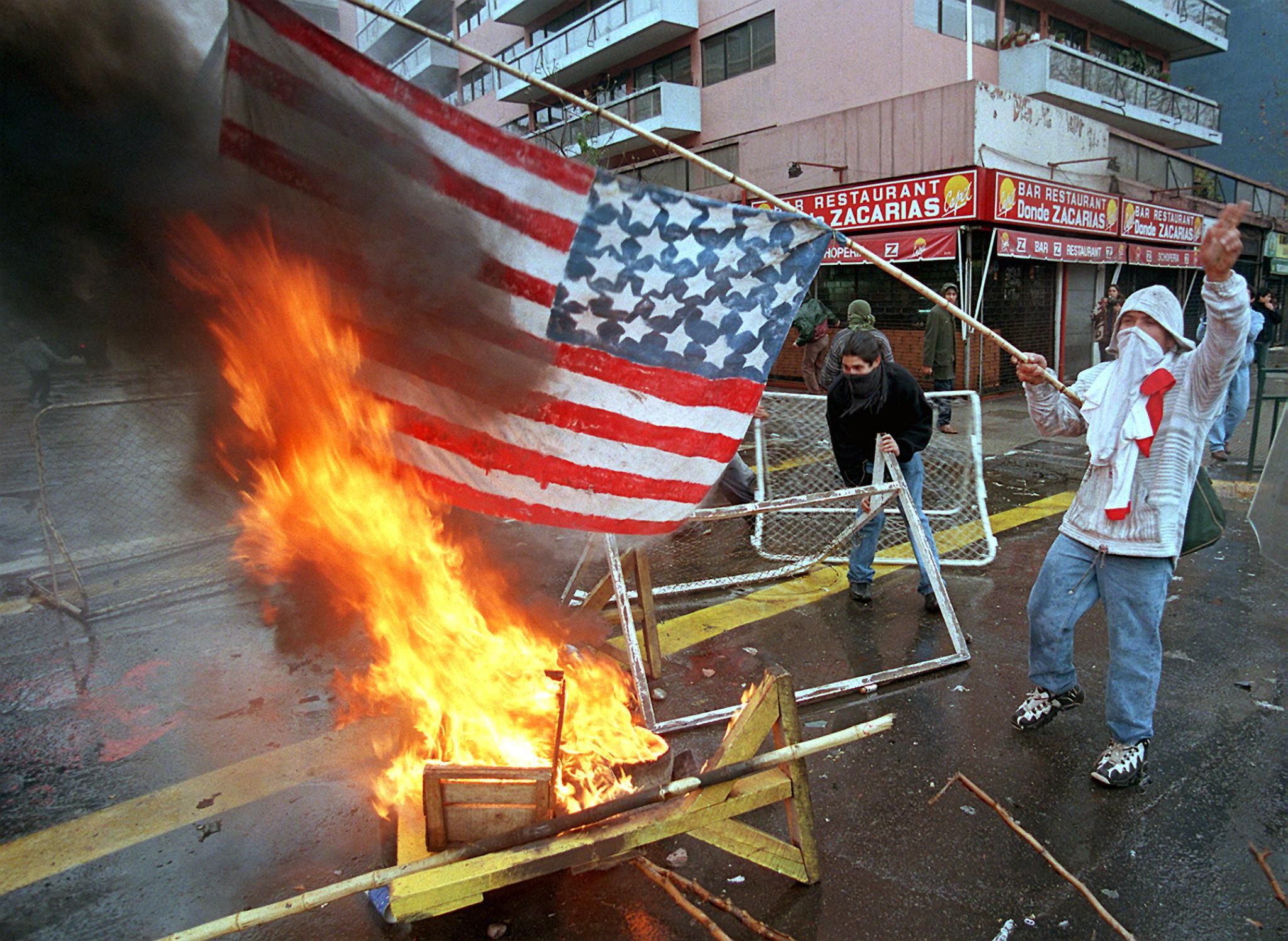 A man burns an American flag in the streets of Santiago, Chile during demonstrations marking the 25th anniversary of the death of Chilean President Salvador Allende.  (Photo by ORLANDO BARRIA / AFP).