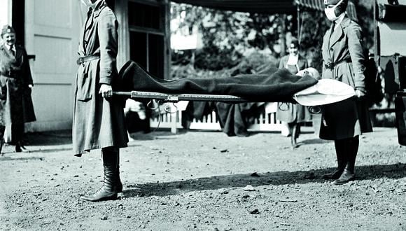 Washington D. C. Dos enfermeras de la Cruz Roja conducen a un paciente durante la pandemia de gripe en 1918, que coincidió con los días finales de la Primera Guerra Mundial. Al frente, un titular de El Comercio de enero de 1919, que llamaba a prevenir la enfermedad. FOTO: Getty Images.