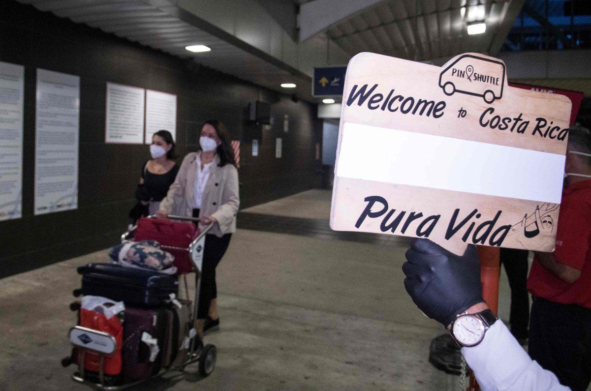 Las personas llegan al aeropuerto Juan Santamaría, donde son recibidas por un operador turístico con un letrero que dice "Bienvenido a Costa Rica, Pura Vida" en San José, el 3 de agosto de 2020. Se trata del primer vuelo comercial que aterriza en el país desde el inicio de la pandemia del coronavirus. (AFP / Ezequiel BECERRA).