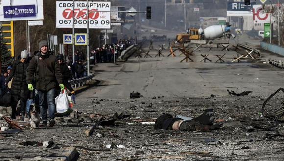 Los residentes pasan junto a un cuerpo que yace en medio de una carretera mientras evacuan la ciudad de Irpin, al norte de Kiev, el 10 de marzo de 2022. (ARIS MESSINIS / AFP).