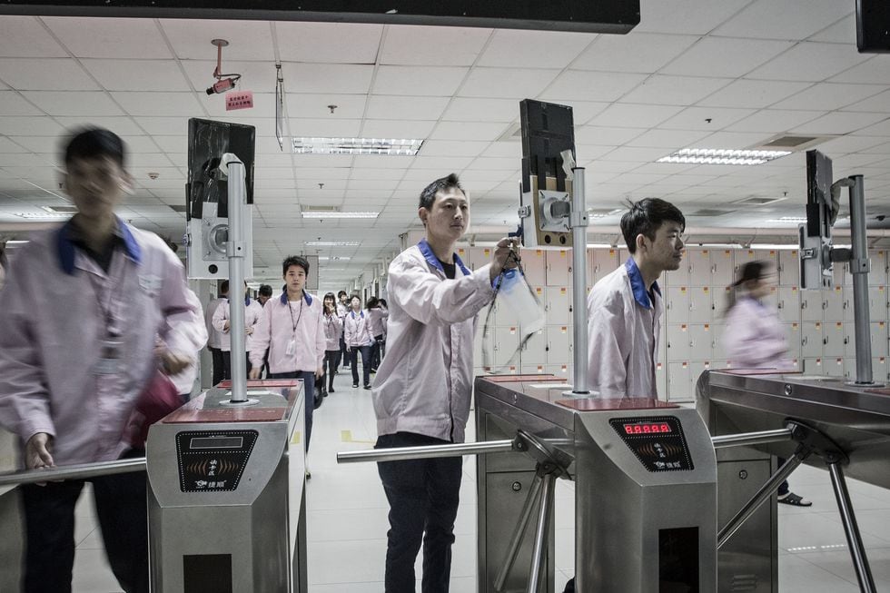 Employees look into facial recognition devices as they swipe their badges to enter the assembly line area at a Pegatron Corp. factory in Shanghai, China, on Friday, April 15, 2016. This is the realm in which the world's most profitable smartphones are made, part of Apple Inc.'s closely guarded supply chain. Photographer: Qilai Shen/Bloomberg