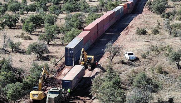 Los trabajadores aseguran uno de una larga fila de contenedores de envío, apilados para crear un muro entre los Estados Unidos y México, en un camión de plataforma para su remoción en el Bosque Nacional Coronado cerca de Hereford, Arizona, el 20 de enero de 2023. (Foto: Robyn BECK / AFP)