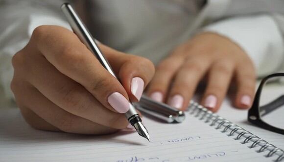 Una mujer escribiendo con un bolígrafo sobre el papel. | Imagen referencial: Pexels