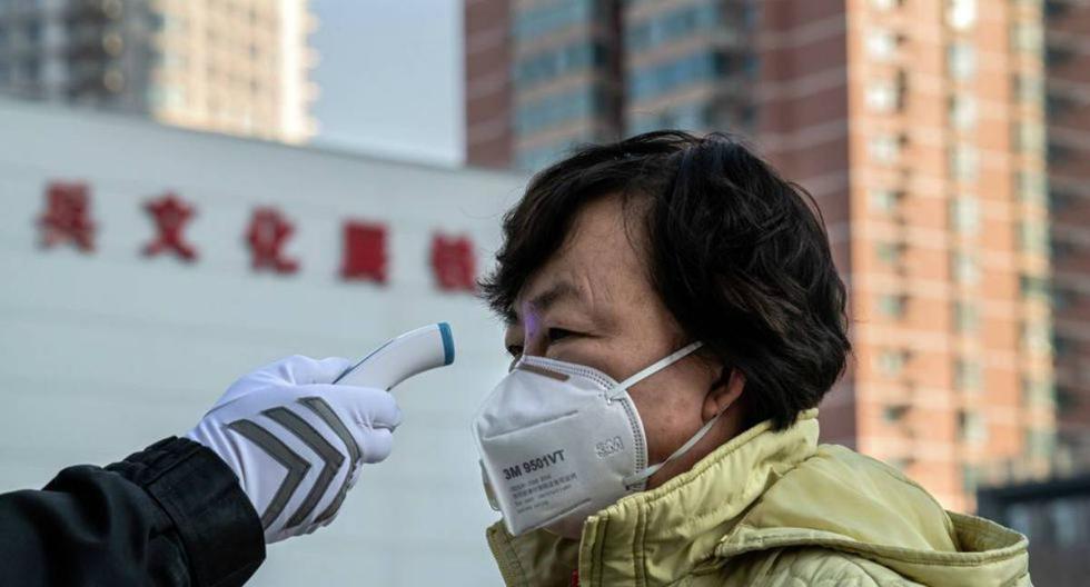 Un guardia verifica la temperatura de una mujer que usa una máscara como medida preventiva tras el brote de coronavirus. (AFP)