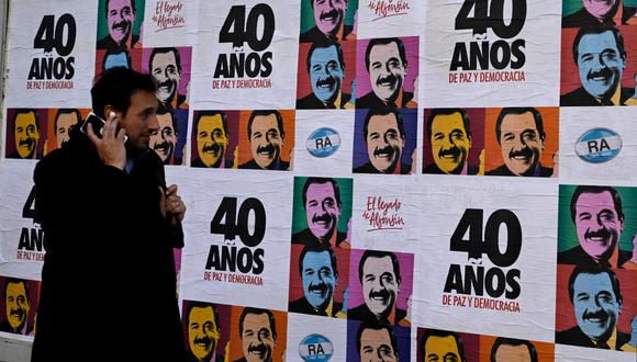 Un hombre camina junto a pancartas alusivas a la celebración del 40 aniversario del retorno de la democracia en Argentina y la elección del fallecido expresidente (1983-1989) Raúl Alfonsín. (Foto de LUIS ROBAYO / AFP).