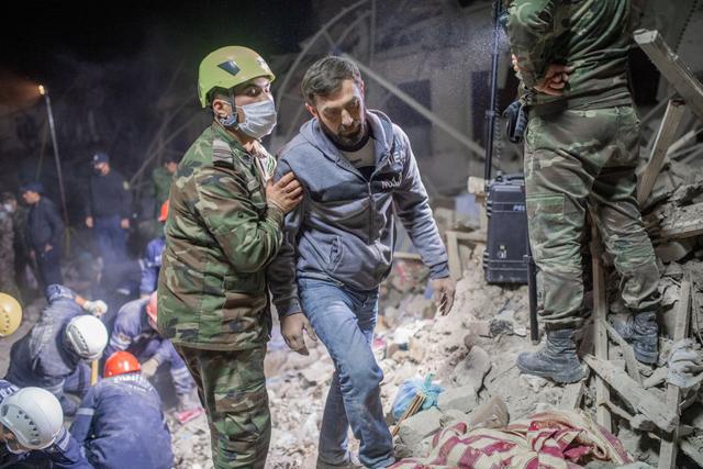 Un trabajador de rescate camina junto a un residente que busca a familiares en un sitio alcanzado por misiles en la ciudad de Ganja, Azerbaiyán. (Foto de Bulent Kilic / AFP).