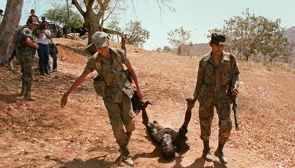 Soldados salvadoreños cargan el cuerpo de un guerrillero muerto en un ataque a una base militar a 180 kilómetros al este de la capital de El Salvador el 1 de marzo de 1989. (Foto de IVAN MONTECINOS / AFP)
